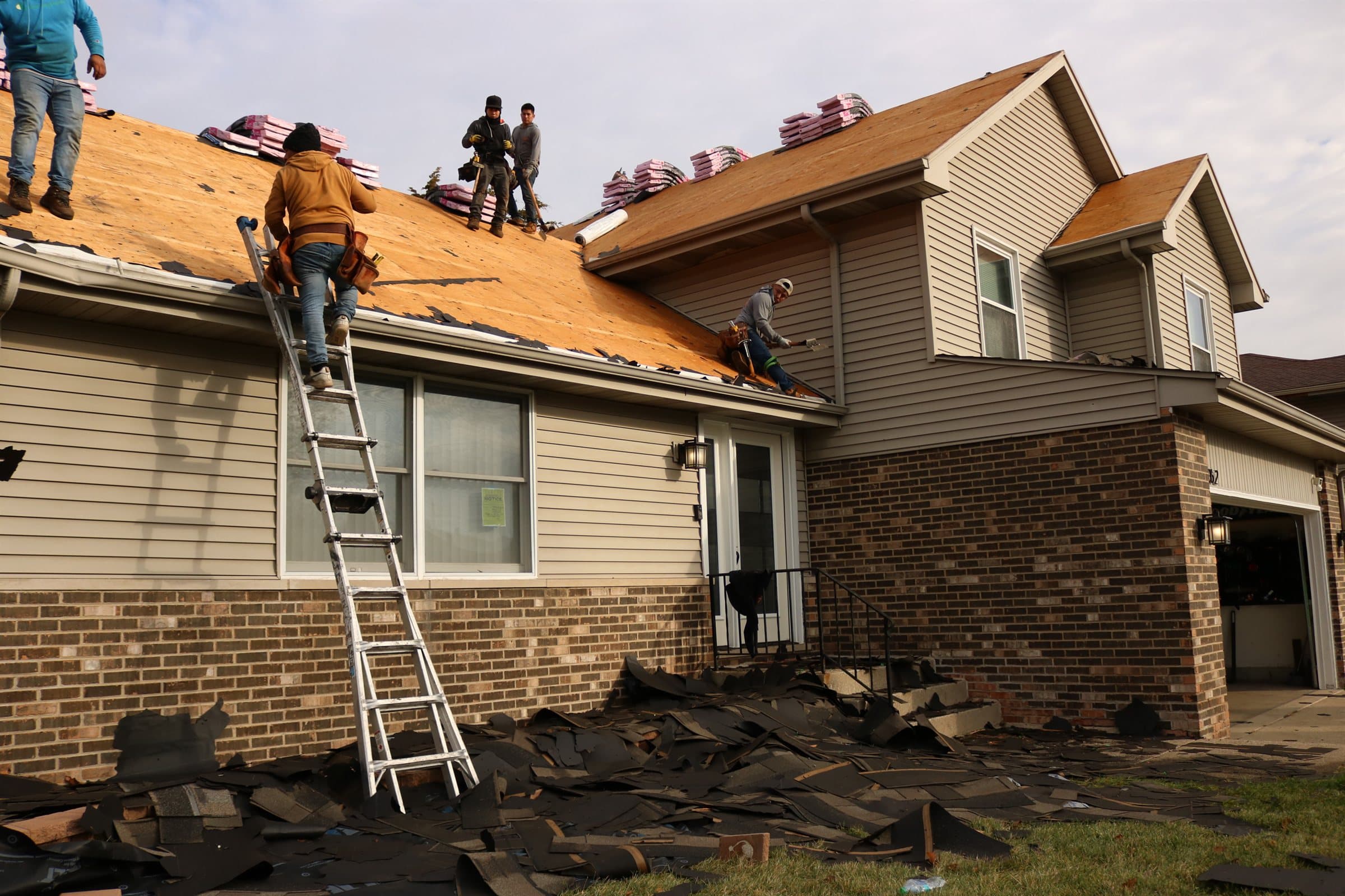 A Revere One roofing crew replacing a roof on a Chicagoland home, decking exposed with new materials staged along the ridge