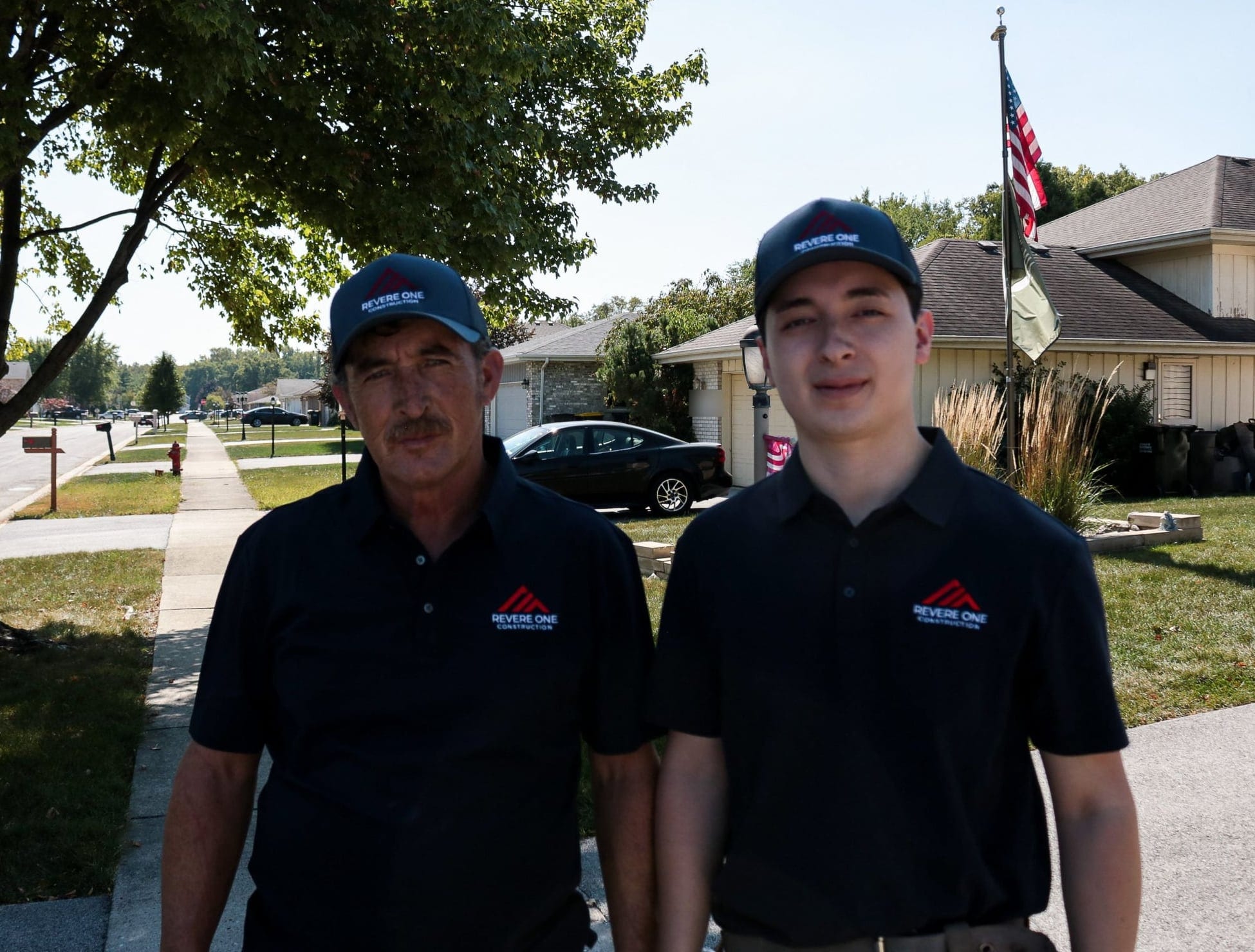 Francisco Jimenez and Francisco Jimenez Jr. of Revere One Construction, father and son, in company polos and caps on a residential street
